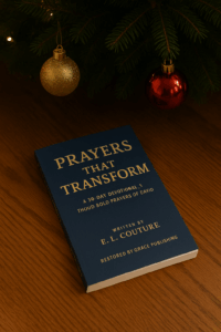 A paperback copy of Prayers That Transform by E. L. Couture resting beneath a decorated Christmas tree with gold and red ornaments, styled as a meaningful Christian Christmas gift to help strengthen faith and transform prayer life.