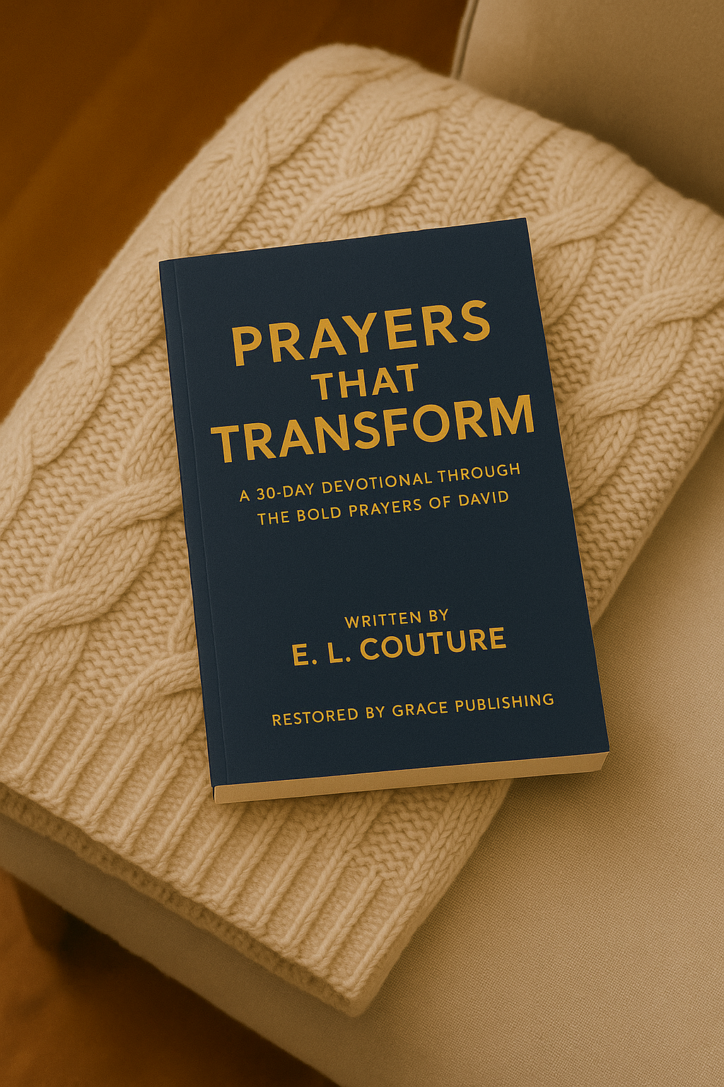 A paperback copy of Prayers That Transform by E. L. Couture resting on a beige cable-knit throw draped over a soft armchair, creating a warm and cozy setting for a Christian devotional Christmas gift that encourages deeper prayer and faith.